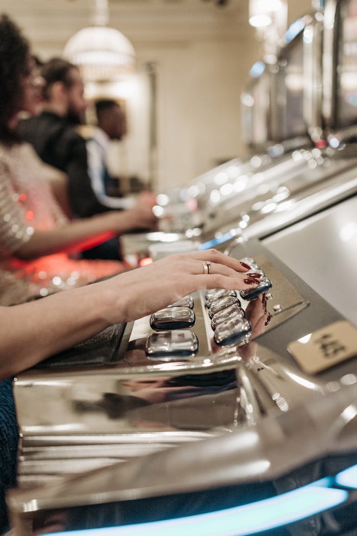 Close-up of people playing slot machines in a casino with a focus on hands pressing buttons.